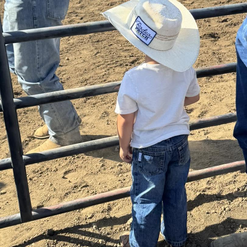 A young rodeo fan at the arena rail wearing a hat with a RodeoPatch patch